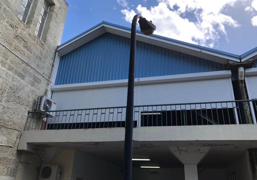 Blue corrugated metal building with a lamp post in front, partially cloudy sky in the background.