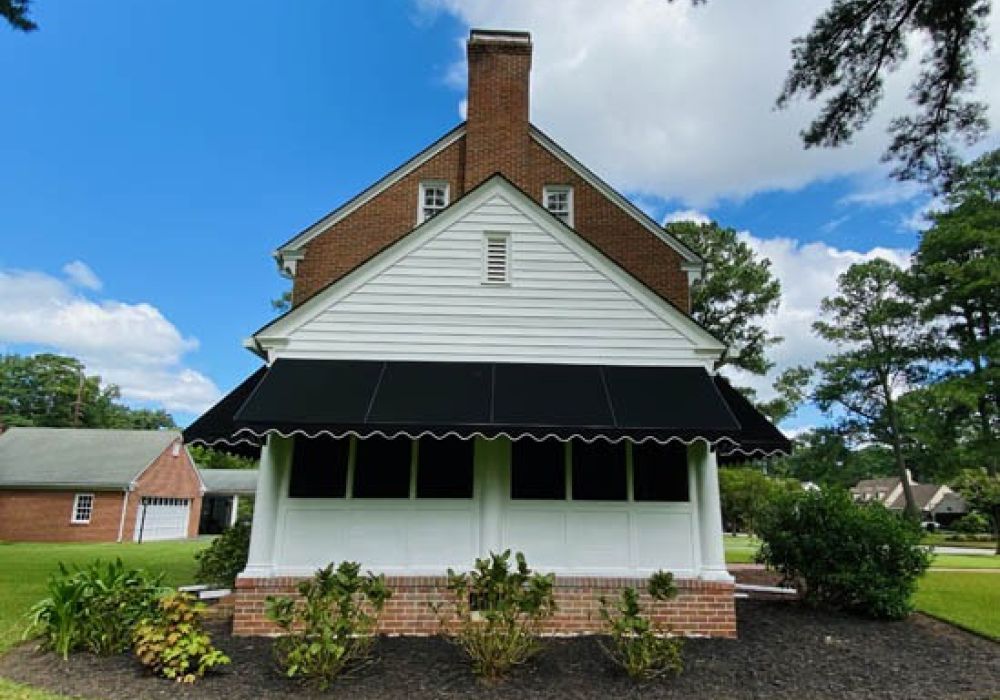 Charming brick house with black awning and lush garden on a sunny day.