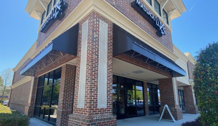 Brick building with dark awnings on a sunny day, showcasing a modern storefront with large glass windows.