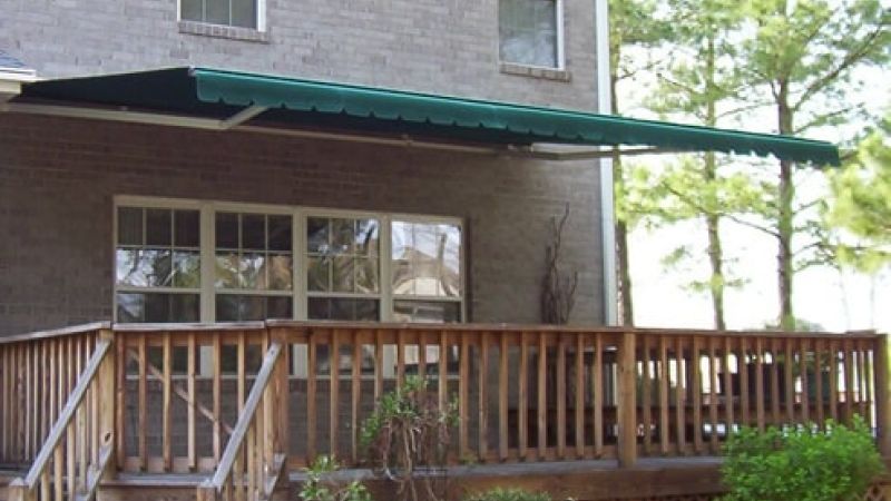 Wooden deck with green awning attached to a brick house, surrounded by trees and plants.