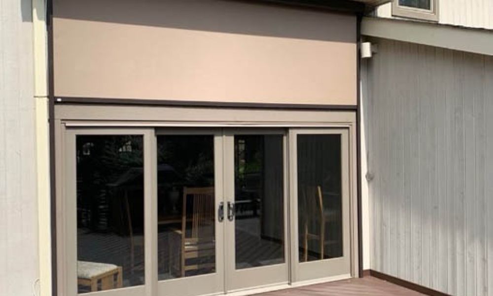 Modern patio with sliding glass doors and retractable awning, surrounded by wooden decking.