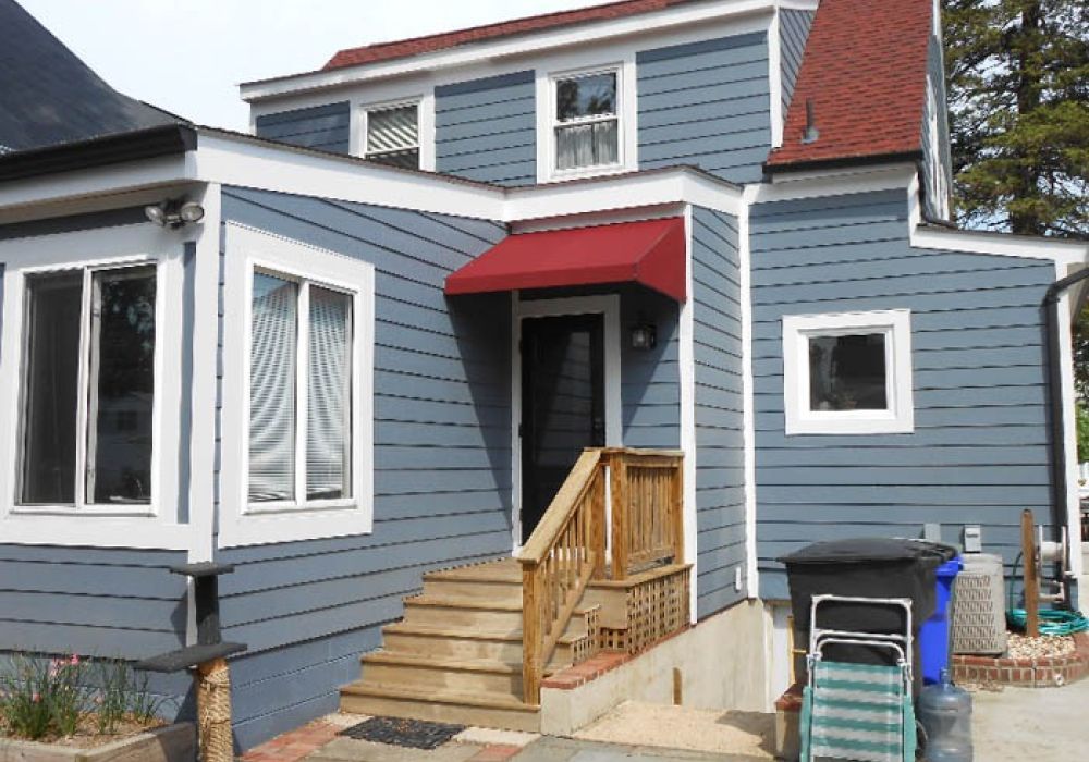 Blue two-story house with a red awning, wooden stairs, and white window frames.