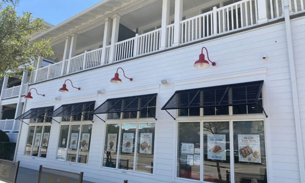 White building with red lamps and large windows displaying posters under black awnings on a sunny day.