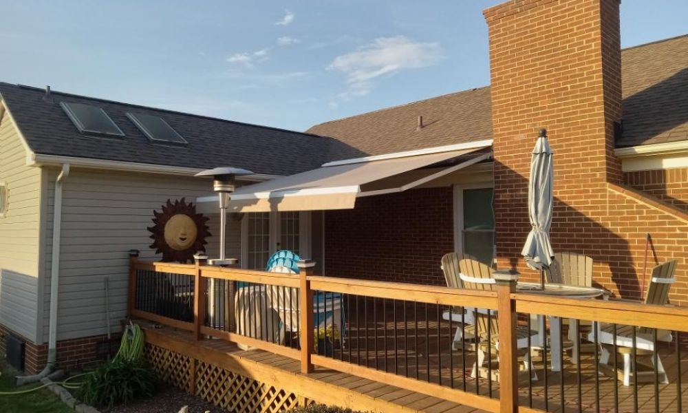 Sunny backyard deck with patio umbrella, chairs, and a retractable awning beside a brick house.