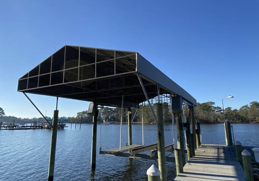 Covered boat lift on a clear day by a wooden dock and calm lake with trees in the background.