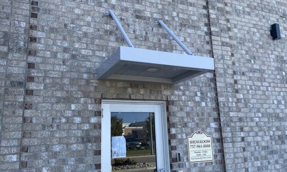 Glass door on brick wall with metal awning and showroom sign. Shadows from sunlight enhance the textured brickwork.