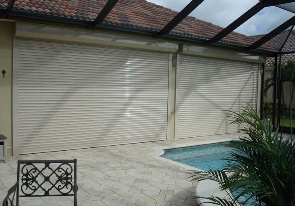 Poolside view of a house with white hurricane shutters under a tiled roof, providing storm protection with elegance.