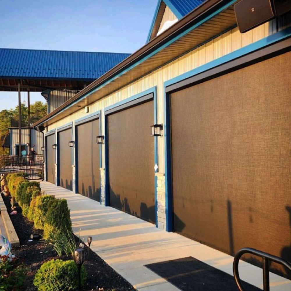Modern building exterior with large brown shades and blue trim, landscaped garden in sunlight.