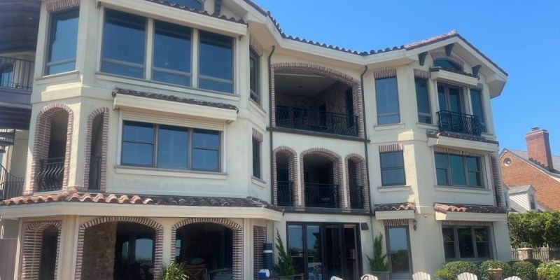 Luxurious three-story villa with balcony and patio seating under a clear blue sky.