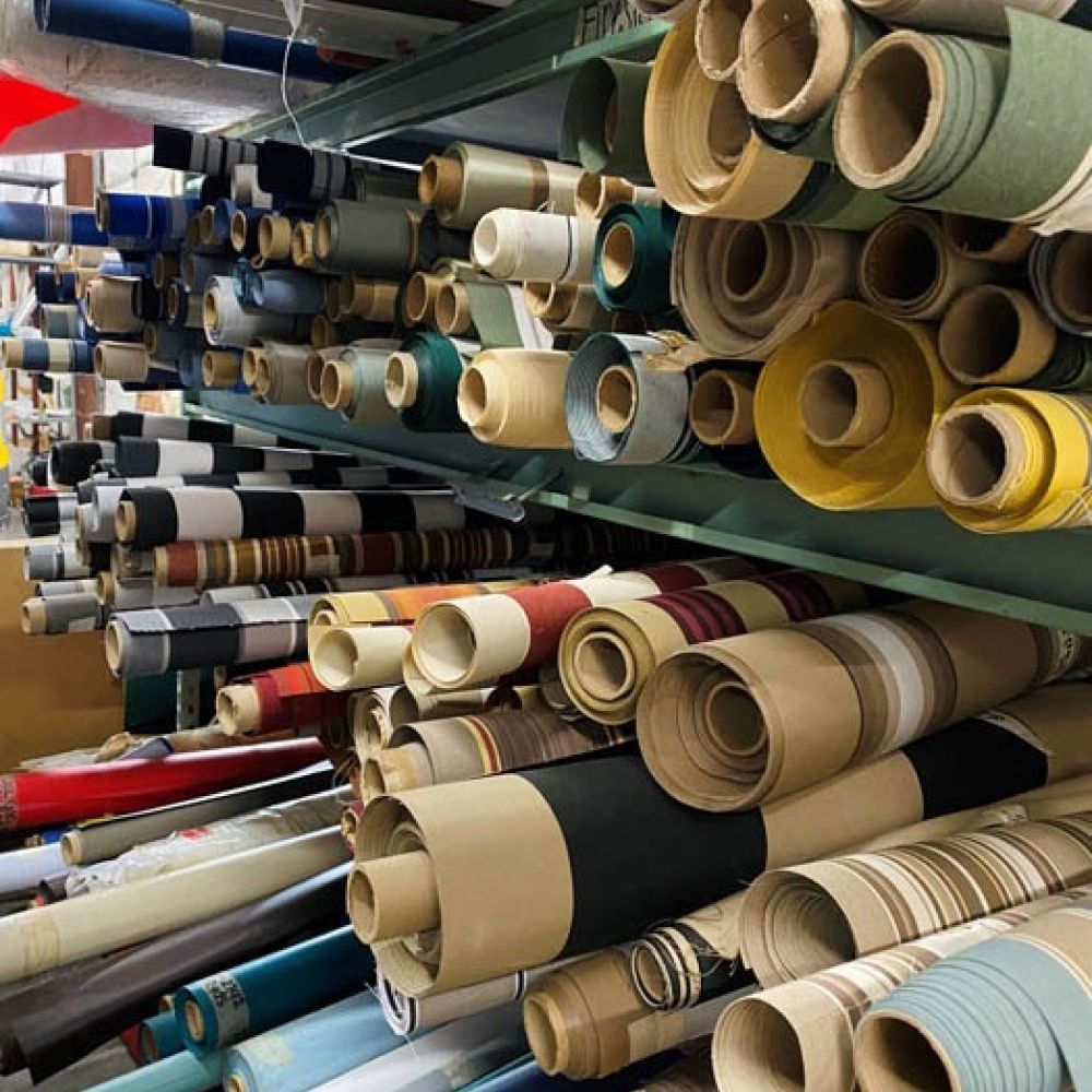 Rolls of colorful awning stacked on shelves, showcasing various patterns and textures in a storage room.