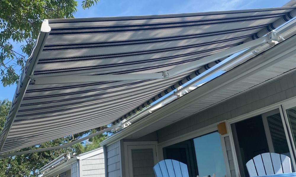 Retractable striped awning over a sunny patio with blue chairs, perfect for outdoor shade and relaxation.