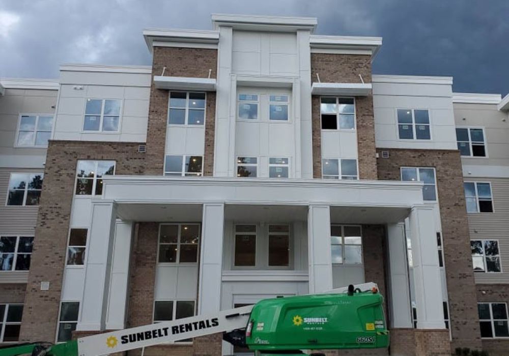 Modern apartment building under construction with green lift equipment in front of a cloudy sky.