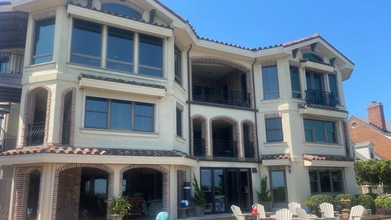 Luxurious three-story villa with balcony and patio seating under a clear blue sky.