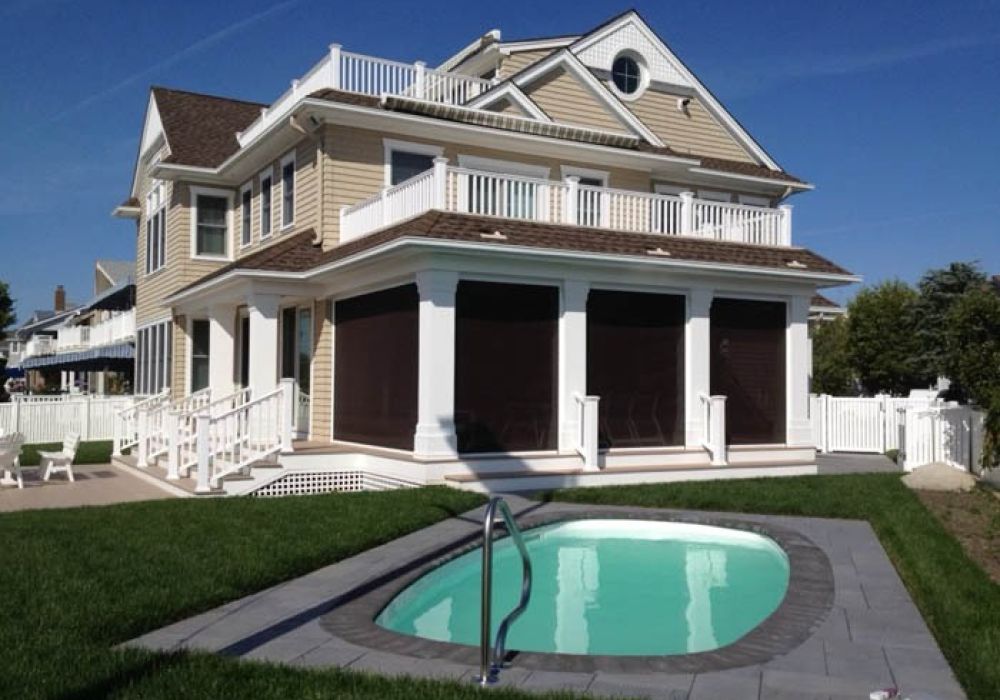 Two-story house with a small backyard pool, surrounded by a white fence under a clear blue sky.
