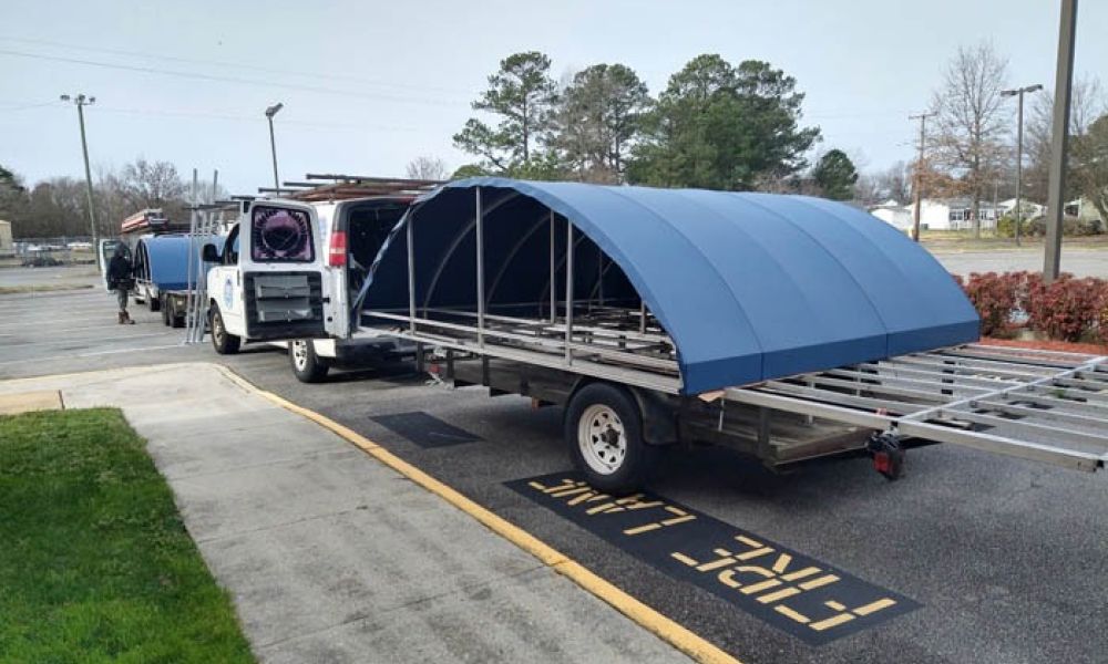 Truck transporting blue metal structure in a parking lot, labeled Fire Lane. Trees in background.