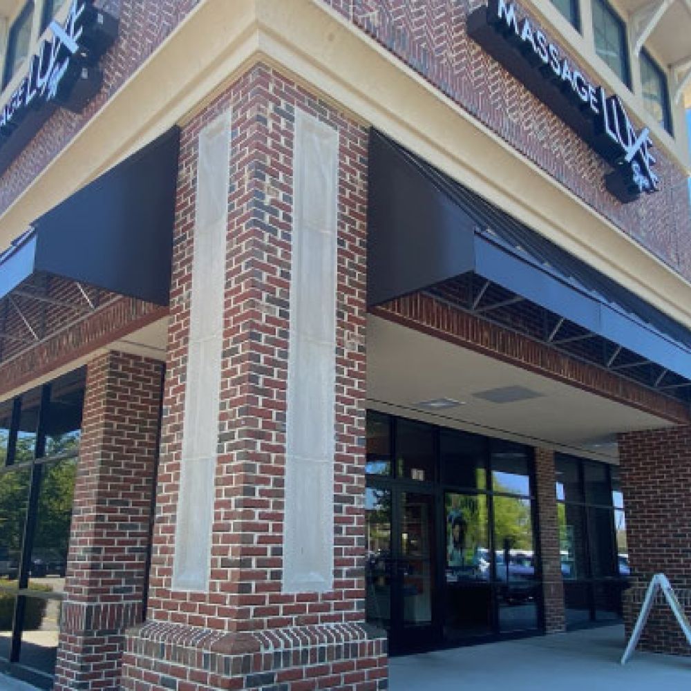 Brick building with dark awnings on a sunny day, showcasing a modern storefront with large glass windows.