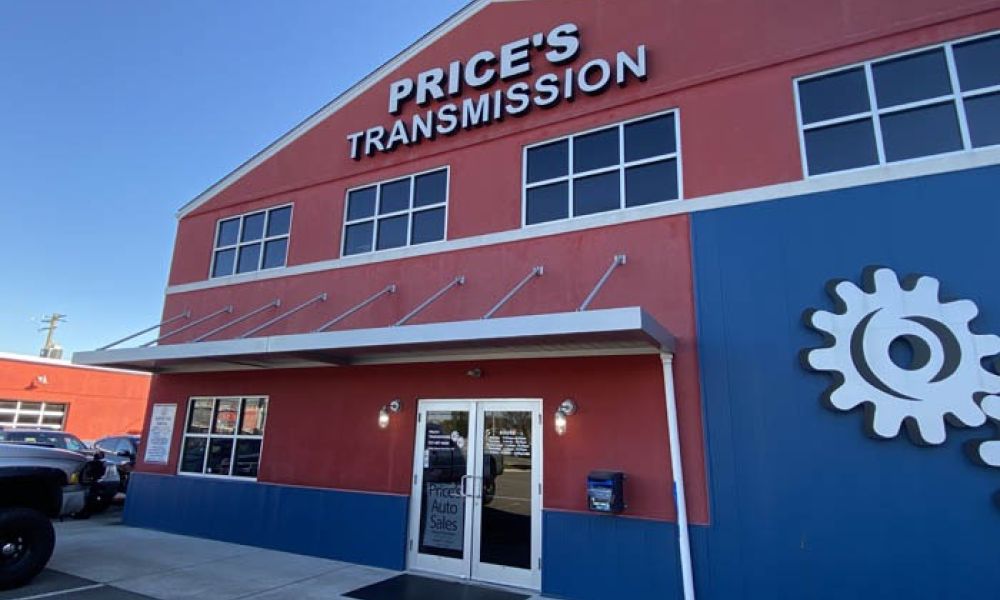 Red and blue building of Price's Transmission shop with logo and parking area in front.