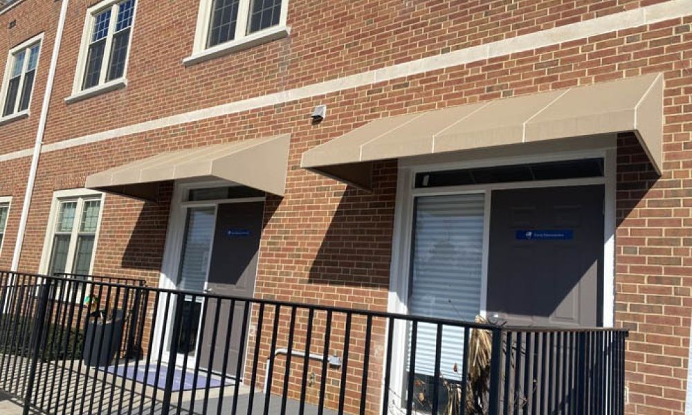 Brick office building with beige awnings, railing, and sunlight on the facade.