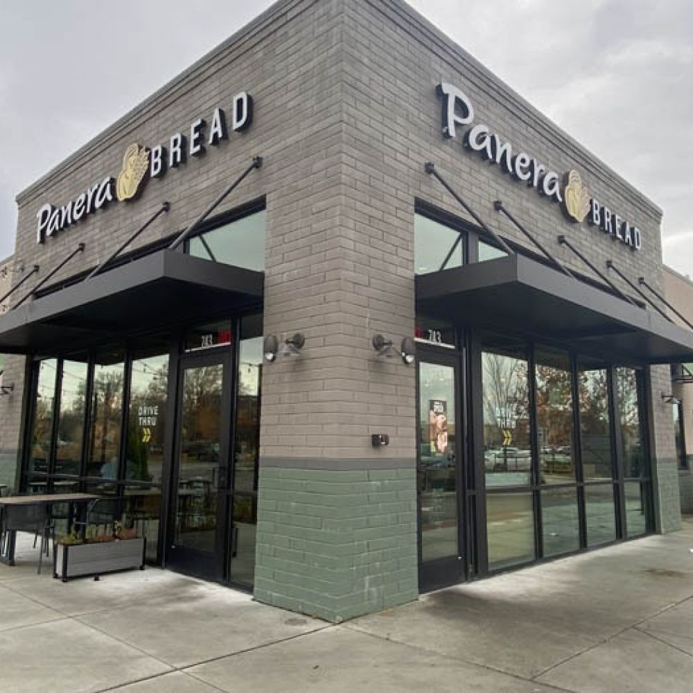 Modern Panera Bread storefront on a cloudy day with outdoor seating area visible.