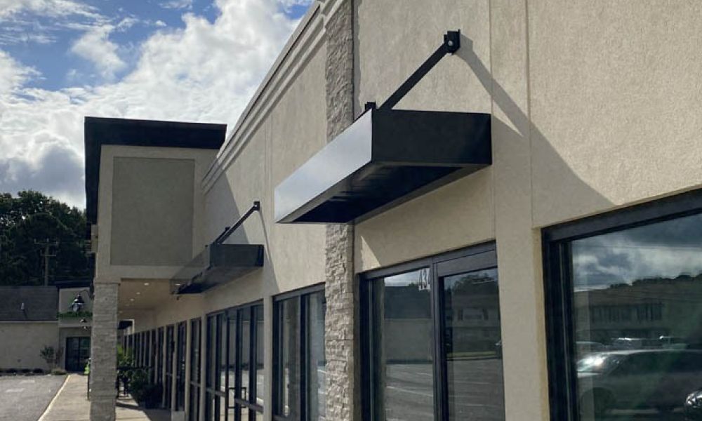 Modern beige commercial building exterior with large windows and awnings under a partly cloudy sky.