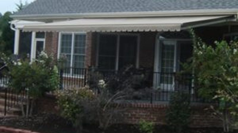 Rear view of a house with retractable awning, brick patio, and garden landscaping.