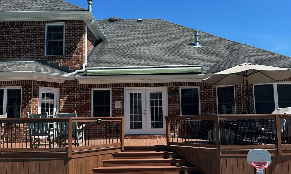 Brick house with wooden deck and pool under clear blue sky, perfect for summer relaxation.