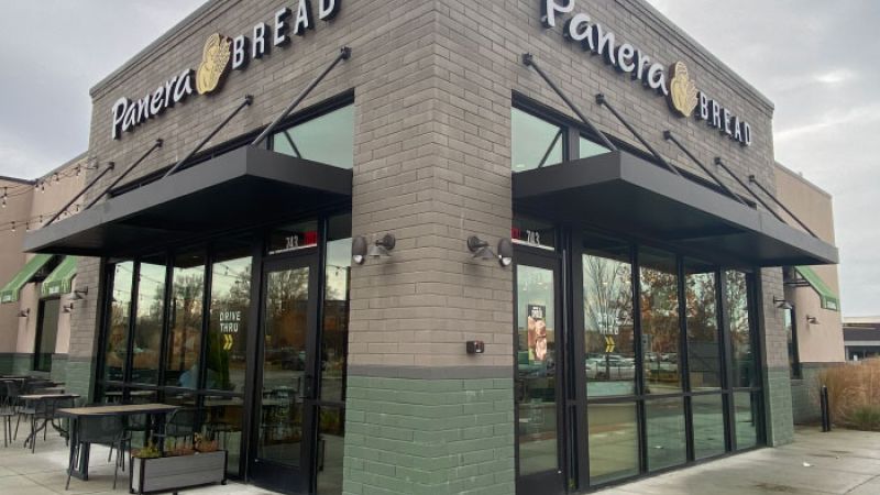 Modern Panera Bread store exterior with glass windows and patio seating, showcasing its inviting design and branding.