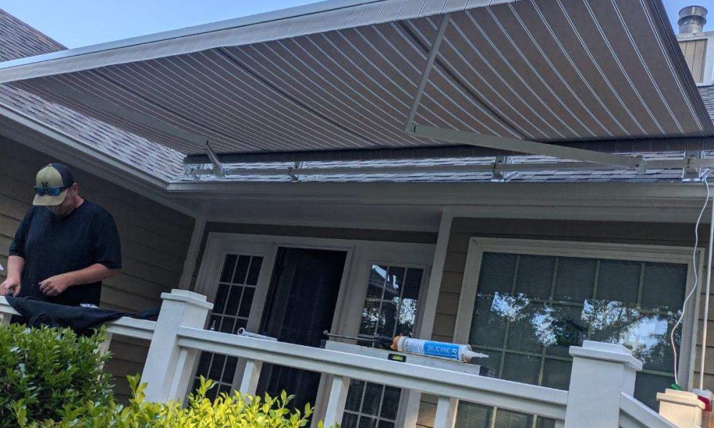 Patio with retractable awning and greenery, person working on installation, sunny day.