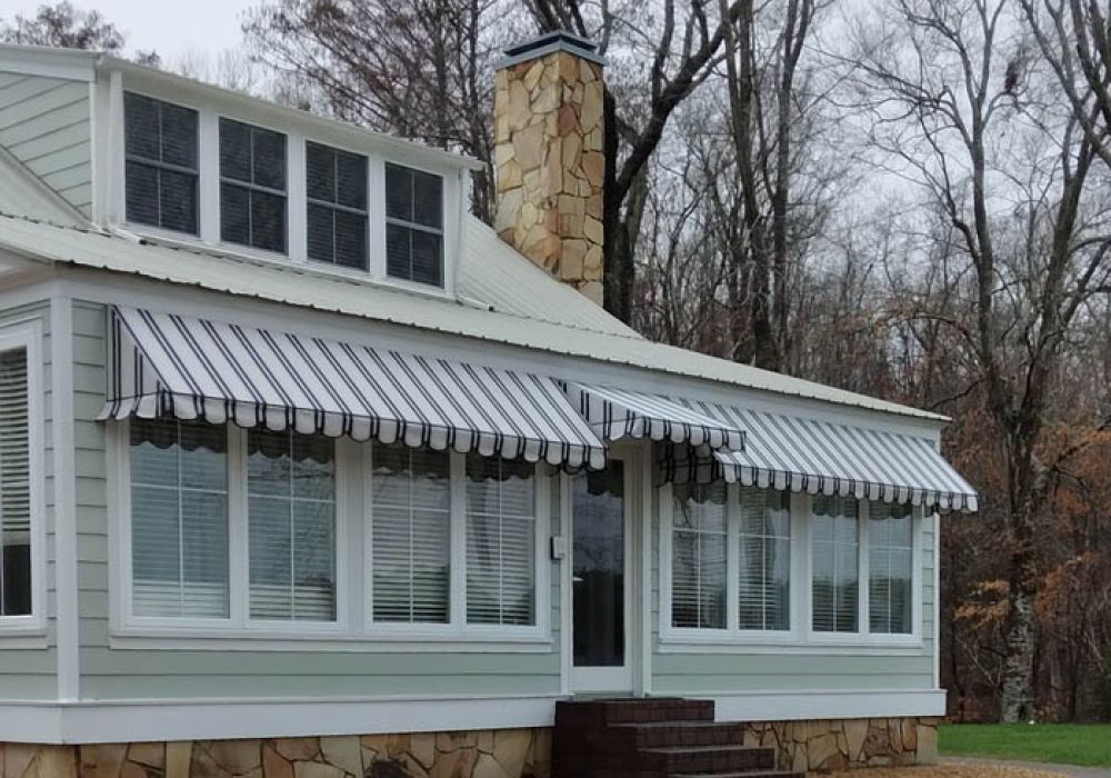 Charming house with striped awnings, surrounded by trees, featuring a stone chimney and large windows. Perfect for cozy living.
