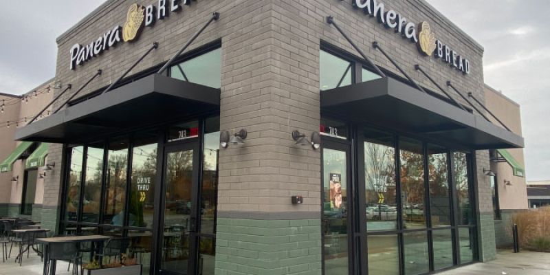 Modern Panera Bread store exterior with glass windows and patio seating, showcasing its inviting design and branding.