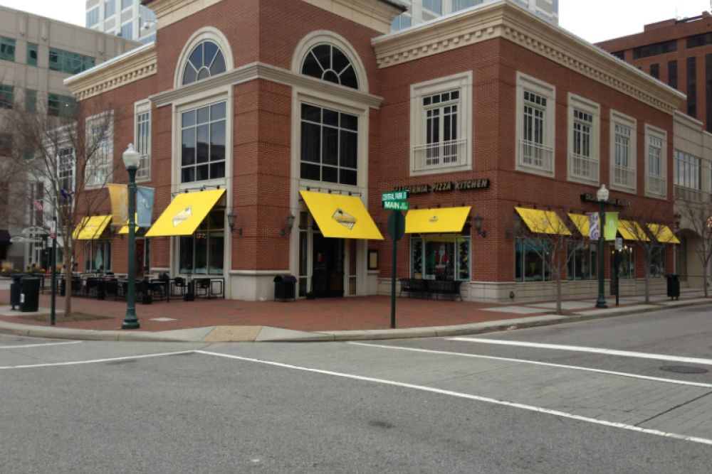Brick building with yellow awnings at street corner, urban setting, restaurant with outdoor seating visible.
