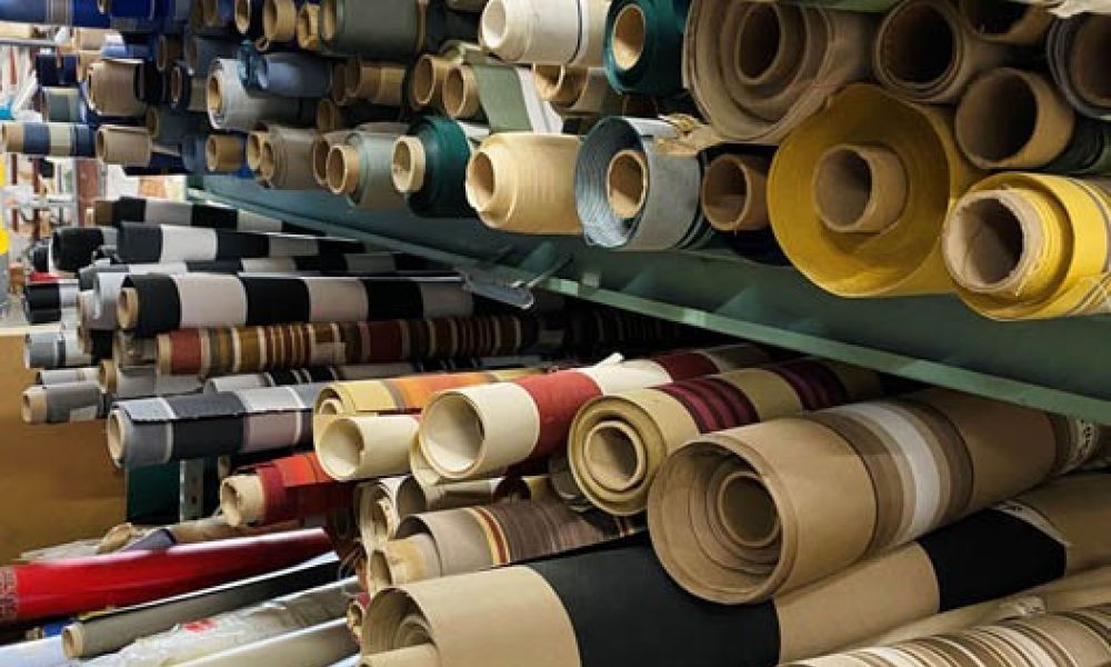 Rolls of colorful awning stacked on shelves, showcasing various patterns and textures in a storage room.