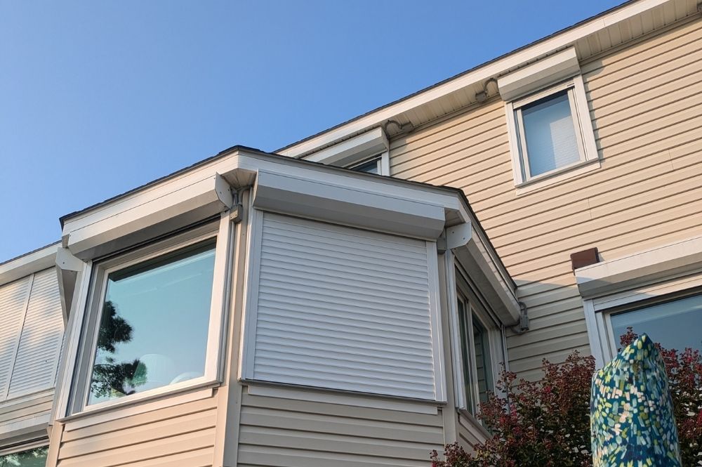 Modern house exterior with beige siding and large windows under a clear blue sky.