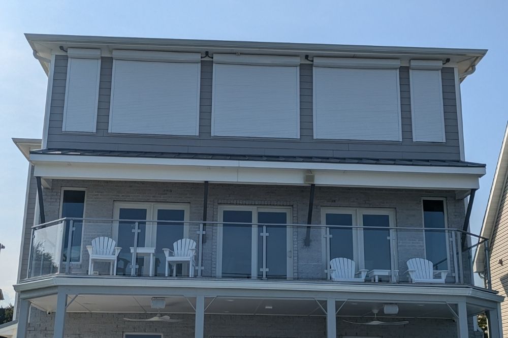 Modern two-story house with glass balcony and white shutters under a clear blue sky.