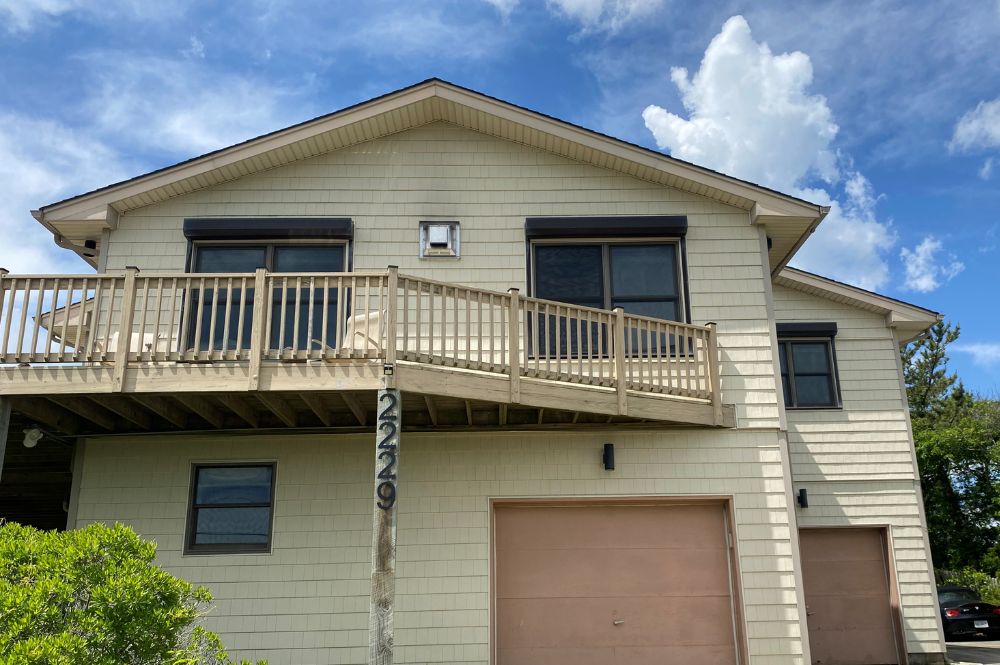 Modern two-story house with a wooden balcony and garage, set under a blue sky with clouds.
