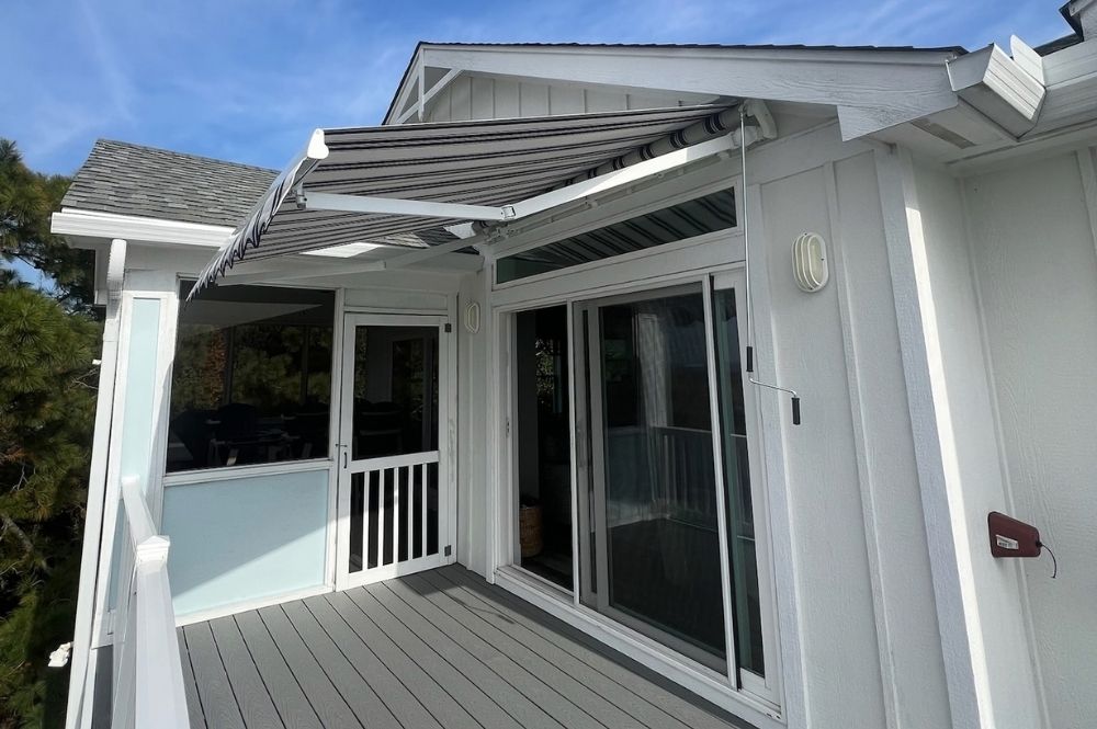 Awning on a house deck with sliding glass doors and white siding under a blue sky.